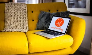 Żółta kanapa z laptopem otwartym na stronie couchsurfing. Obok koc i szara poduszka.