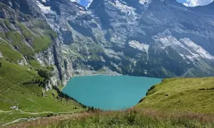 Türkisblaue Oeschinensee Schweiz, umrahmt von steilen, grünen Berghängen und schneebedeckten Gipfeln. Ein idyllischer Ort für Wanderer.