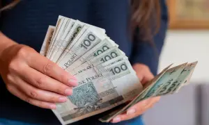 Dłonie trzymające stos banknotów 100 zł. Czy to przedpłata, czy zaliczka? Decyzja o płatności.