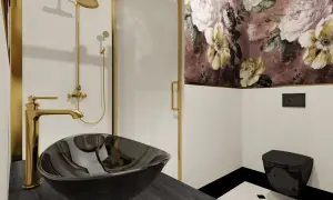 Elegancka łazienka glamour z czarną umywalką, złotą armaturą i tapetą w kwiaty.