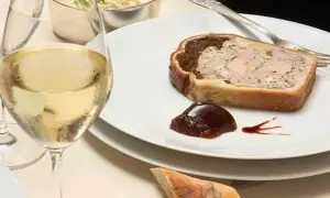Une tranche de pâté en croûte, garnie de confiture de figues, accompagnée d'un verre de vin blanc et d'une coupelle de crudités.