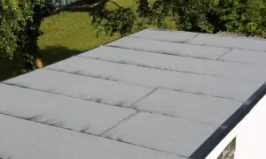 Graues Garagendach mit sichtbaren Rissen und Spalten, die auf ein undichtes Garagendach hindeuten. Im Hintergrund grüner Rasen und Bäume.