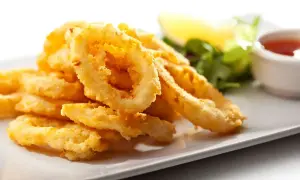 Anelli di totano dorati e croccanti, cotti in friggitrice ad aria, serviti su un piatto bianco con contorno di insalata e salsa.