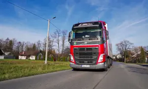 Czerwona ciężarówka Volvo z naczepą jedzie drogą. To praca spedytora, kod zawodu 334101.