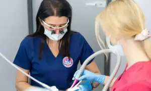Dentystka z lupami i maską przygotowuje znieczulenie dentystyczne skład. Asystentka trzyma ssak.