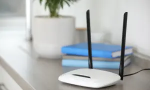 Biały router z dwiema antenami, zapewniający szybkie **standardy wifi**. W tle książki i roślina w doniczce.