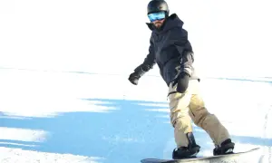 Mężczyzna w kasku i goglach zjeżdża na snowboardzie. Zastanawiasz się, ile kosztuje wypożyczenie snowboardu?