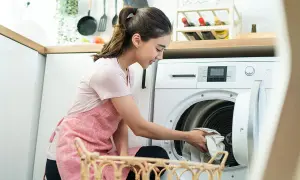 Frau lädt Wäsche in die Waschmaschine. Sie fragt sich, wie oft Jeans waschen, um sie frisch zu halten.