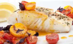 Pyszny halibut ryba, pieczony z pomidorkami koktajlowymi i ziołami, podany z plasterkami cytryny.