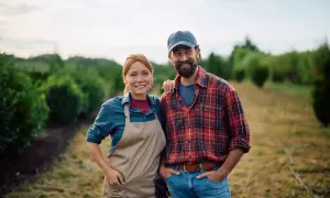 Szczęśliwa para rolników na tle plantacji. Zastanawiają się, ile kosztuje dopisanie żony do działki.