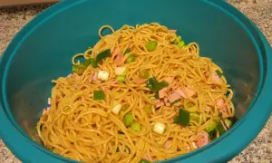Ein leckerer Maggi Salat mit Spaghetti, Schinkenwürfeln und Frühlingszwiebeln in einer blauen Schüssel.