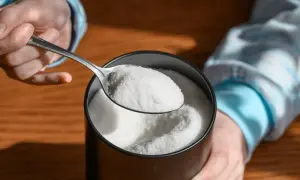 Mano che preleva eritritolo con un cucchiaio da un contenitore. Cos'è l'eritritolo? Un dolcificante a basso contenuto calorico.
