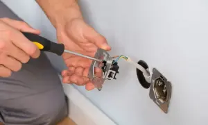 Ręce majsterkowicza przykręcają śrubokrętem mechanizm gniazdka. Trwa zerowanie gniazdka, przygotowanie do montażu.