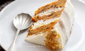 Una fetta di torta di carote, soffice e ricca, con glassa bianca e noci tritate.