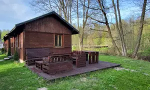 Drewniana chata z meblami na tarasie, otoczona zielenią i lasem. Idealne miejsce na agroturystykę w pobliżu.