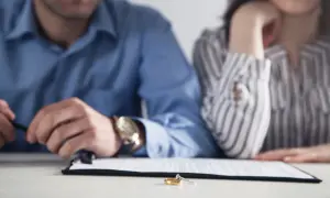 Para, która siedzi przy stole, z obrączkami na pierwszym planie. Zastanawiają się, ile się czeka na odpis wyroku rozwodowego.