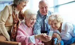 Cztery starsze osoby śmieją się, patrząc na telefon. Może właśnie sprawdzają, jak sprawdzić kolejkę do sanatorium z NFZ.
