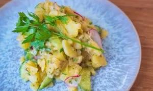 Ein köstlicher Kartoffelsalat mit Gurken, Radieschen und frischer Petersilie auf einem blauen Teller.