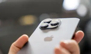 Dłoń trzyma iPhone 14 Pro, pokazując jego potrójny aparat. Długi czas pracy na baterii pozwala na swobodne korzystanie.