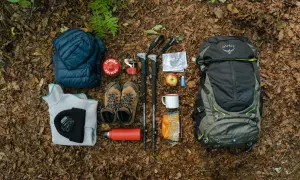 Préparation pour faire son sac de randonnée à la journée : sac à dos Osprey, chaussures, vêtements chauds, bâtons, réchaud, gourde, carte et en-cas.