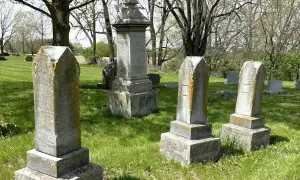 Vieilles pierres tombales dans un cimetière verdoyant, sous des arbres feuillus. Un lieu paisible pour se souvenir.