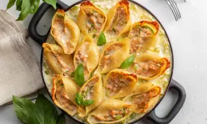Un plat de conchiglioni farcis, dorés et garnis d'une farce savoureuse, baignant dans une sauce crémeuse et décorés de feuilles de basilic frais.