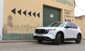 Vit Mazda CX-5 framför en sliten gul byggnad med svarta pilar. Kanske ett Mazda CX-5 problem med att hitta rätt väg?
