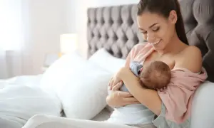 Uśmiechnięta mama karmi piersią noworodka. Czas karmienia jest elastyczny, ważne by dziecko było najedzone.