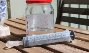 En spruta med koksaltlösning för barn står bredvid ett glas med vatten.