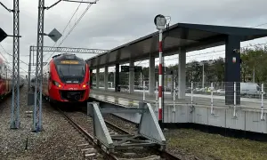 Czerwony pociąg PKP SKM stoi na peronie. W tle nowoczesna wiata i słup sygnalizacyjny.
