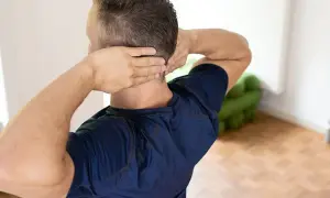 Mann mit Händen im Nacken, der sich fragt: nackenschmerzen wann zum arzt.
