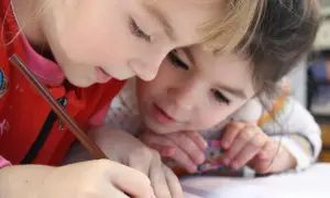 Dwie dziewczynki pochylone nad zeszytem, jedna pisze ołówkiem.