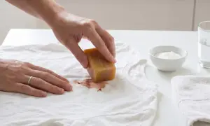 Hand reibt mit Kernseife über Blutfleck auf weißem T-Shirt. So lässt sich blut aus kleidung entfernen.