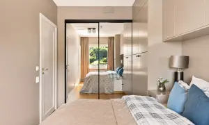 Ein großer spiegel im schlafzimmer reflektiert das Bett, die Vorhänge und das Fenster mit Blick ins Grüne.