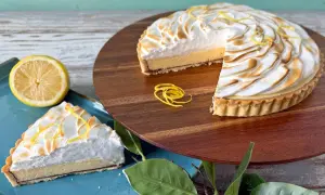 Ein köstliches Zitronentarte Rezept: Ganze Tarte und ein Stück mit Baiserhaube, garniert mit Zitronenzesten.