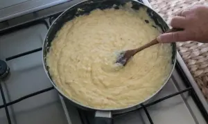 Masa de croquetas cremosa en sartén, removida con cuchara de madera.