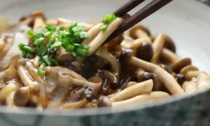 Chopsticks podnoszą pyszne grzybki chińskie w sosie, posypane szczypiorkiem.