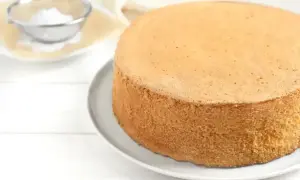 Idealny biszkopt, by wyszedł puszysty, piecz w temperaturze 170-180°C. Na talerzu leży złocisty biszkopt, obok sitko z cukrem pudrem.