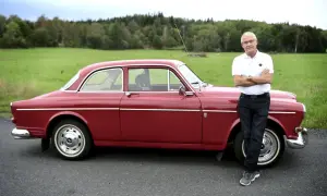 Man i vit pikétröja och jeans lutar sig mot en röd amazon bil.