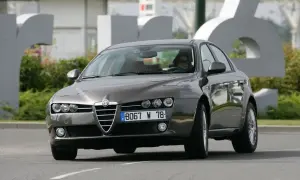 Eleganckie Alfa Romeo 159 2.4 JTDm w kolorze grafitowym, z kobietą za kierownicą, jedzie po drodze.