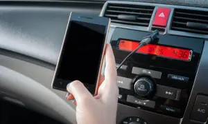 Ręka trzyma smartfon, podłączony kablem do radia samochodowego. Dowiedz się, jak połączyć się z transmiterem.