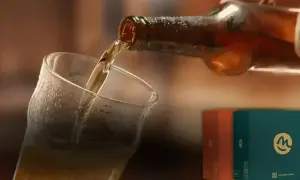 Versando una hefe birra dorata in un bicchiere bagnato. Sullo sfondo, due scatole colorate con il logo "m".