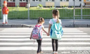Dwie dziewczynki z plecakami idą przez pasy. Od ilu lat dziecko może samo chodzić po mieście? Zależy od dziecka i jego dojrzałości.