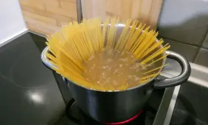Długie, żółte spaghettini gotują się w garnku na kuchence.