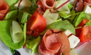 Wykwintna sałatka z szynką parmeńską, pomidorami, serem pleśniowym i świeżymi liśćmi sałaty, polana sosem balsamicznym.