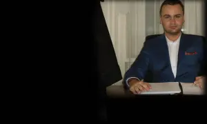 Mężczyzna w garniturze siedzi przy biurku i podpisuje dokumenty.