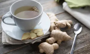 Kubek z herbatą imbirową, plasterki imbiru i korzenie. Czy imbir można pić codziennie? Odpowiedź może być w tym naparze.