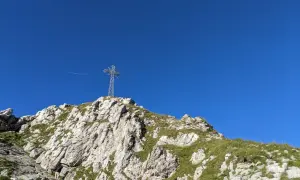 Kamienista trasa na Giewont z krzyżem na szczycie. W tle błękitne niebo i samolot.