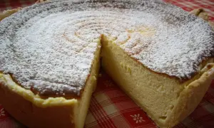 Une délicieuse tarte au fromage blanc, saupoudrée de sucre glace, prête à être dégustée sur une nappe à carreaux rouges.