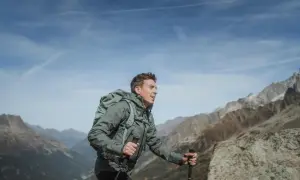 Mężczyzna z plecakiem i kijkami trekkingowymi wędruje po górach, podziwiając widok na masyw Mount Blanc.